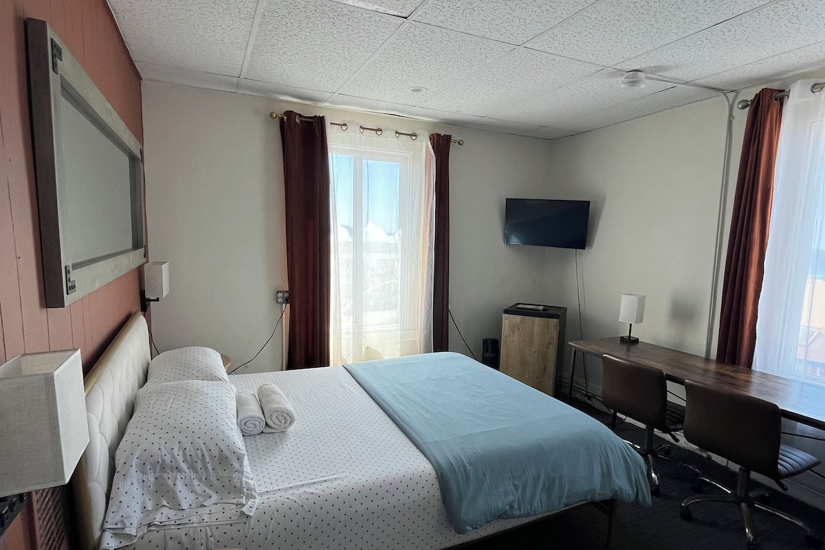 A hotel room with a bed, a desk, a TV, and a small round table.