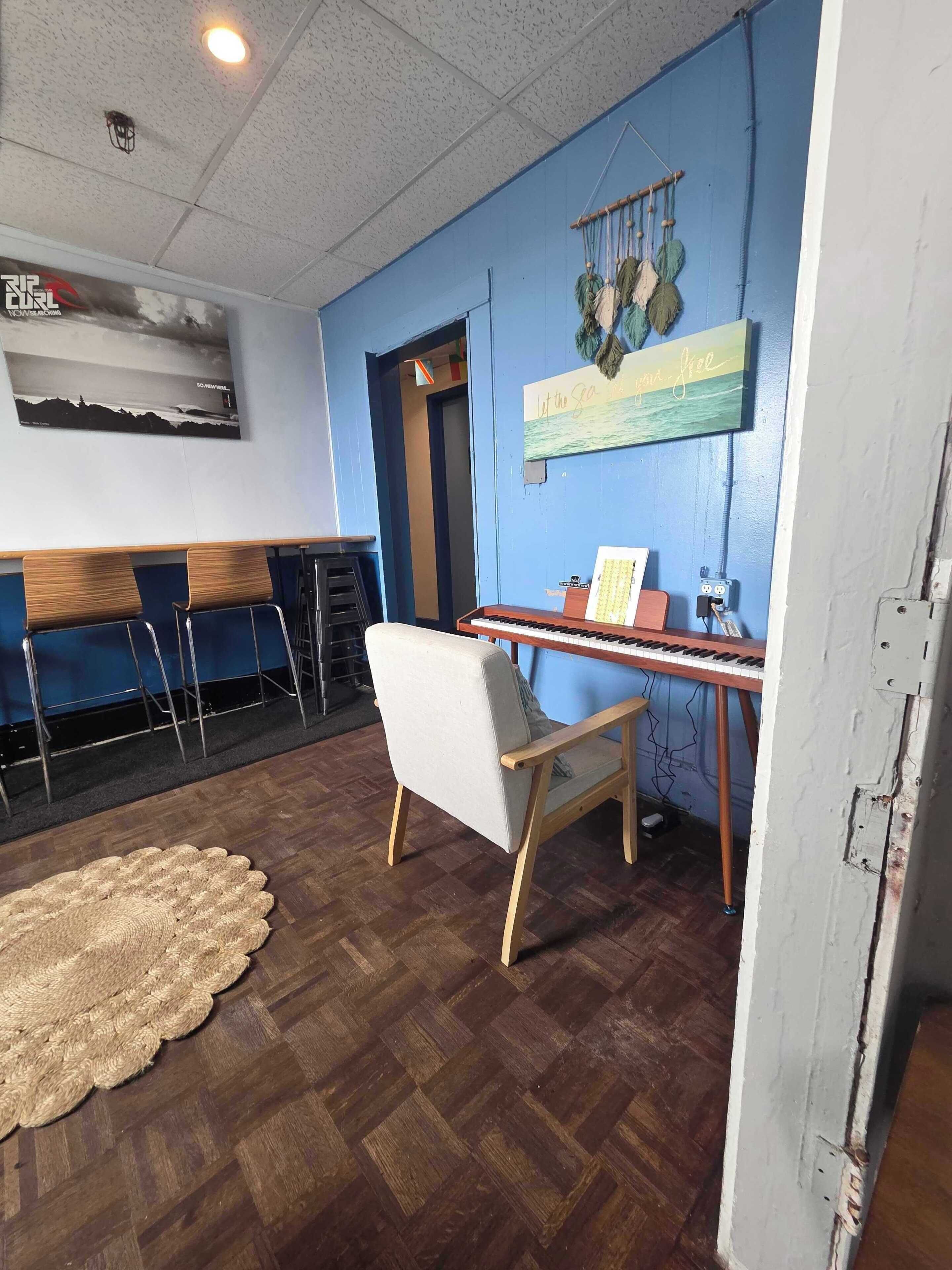 A room with a blue wall, a piano, a chair, and a woven rug.