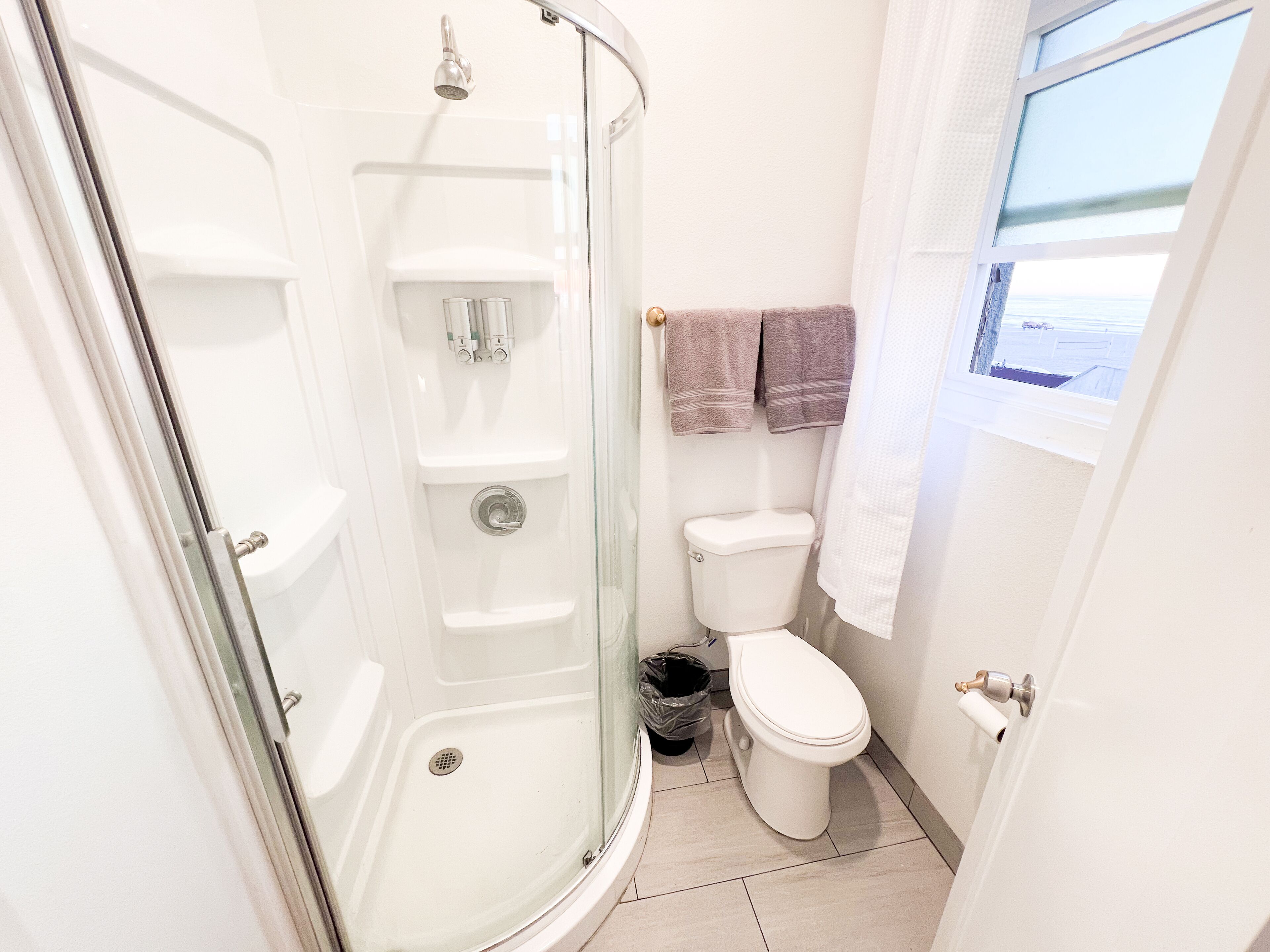 A bathroom with a glass-enclosed shower, a toilet, and a window with a view.