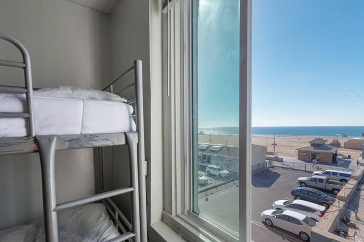Une chambre avec des lits superposés et une grande fenêtre donnant sur un parking et la plage.