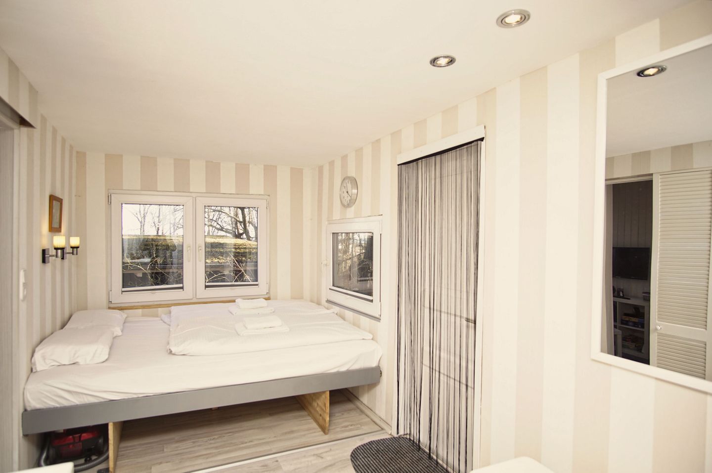 A bedroom with a bed, two windows, a clock, and a wardrobe.