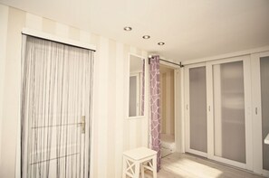Ein Zimmer mit Schiebetür, einem kleinen Tisch, einem Kleiderschrank und einem Duschbereich.