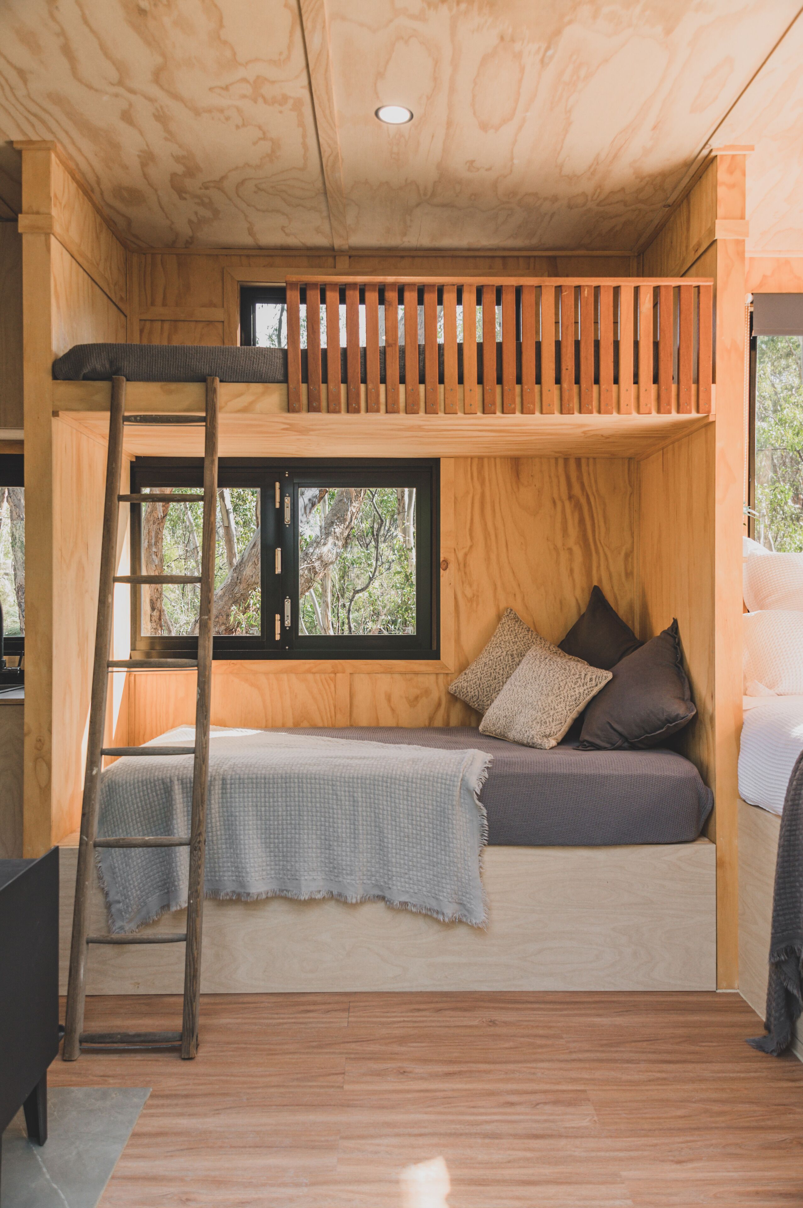 Une petite pièce en bois, équipée d’un lit superposé, d’une échelle et d’une fenêtre donnant sur les arbres.