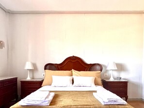 A neatly made bed with a wooden headboard, two bedside tables with lamps, and a plain wall.