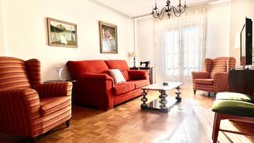 Una sala de estar con un sofá rojo, dos sillones a rayas, una silla verde, una mesa de centro de madera y una araña.