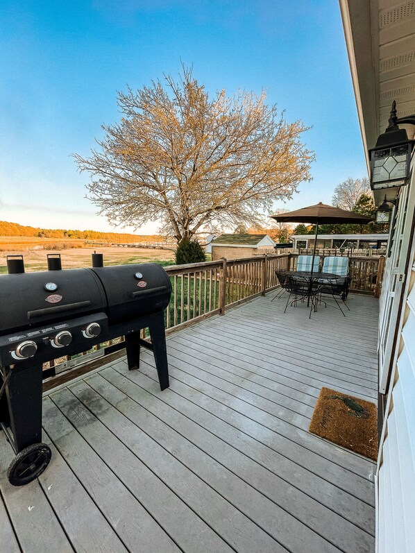 A wooden deck with a barbecue grill, outdoor furniture, and a view of a tree and distant landscape.