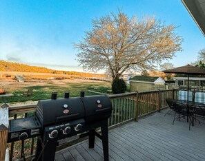A barbecue grill on a wooden deck with a view of a tree and a distant landscape.