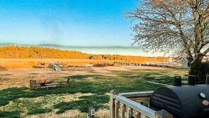 Una terraza con una parrilla y mobiliario exterior, con vista a un campo cubierto de césped y un área boscosa.