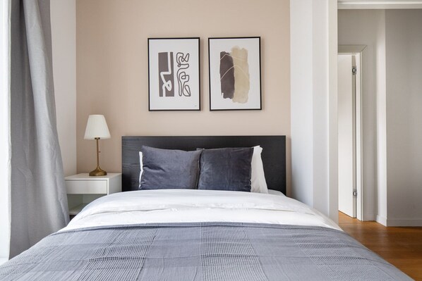 A bedroom with a bed, a nightstand, a lamp, and two framed artworks on the wall.