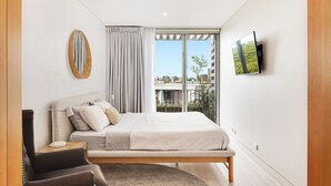 A modern bedroom with a bed, a chair, a TV, and a window with a city view. - Bellevue Hill Designer, Beaches, City & Views (Bellevue Hill)