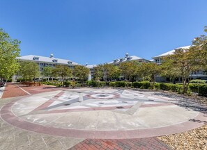 A courtyard with a geometric tile design, surrounded by trees and buildings with a flat roof. - Mini Weeks Stays Available Sunset Island 37 Founta (Ocean City)