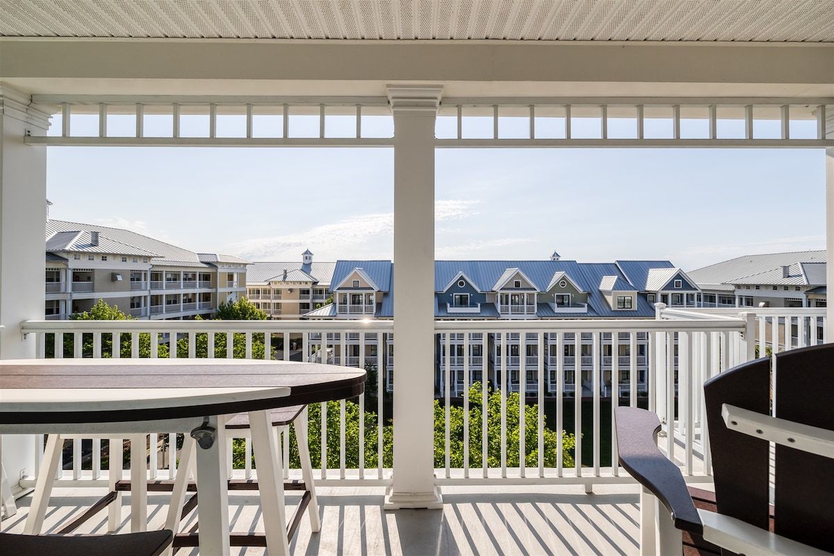 A balcony with a table and chairs, overlooking a row of houses with blue roofs.