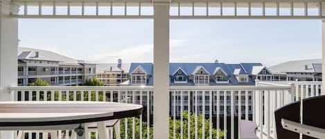 A balcony with a table and chairs, overlooking a row of houses with blue roofs.