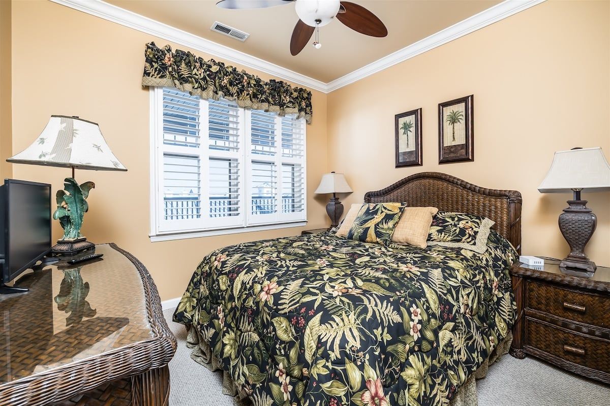 A bedroom with a bed, a television, a desk, and a window with shutters.