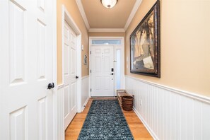 A hallway with white doors, a patterned rug, a framed picture on the wall, and a basket on the floor.