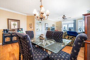 A dining area with a glass table and patterned chairs, a chandelier, and a ceiling fan.
