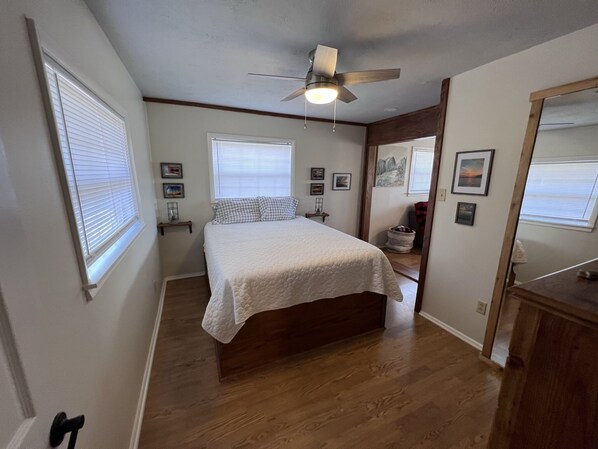 Une chambre à coucher avec un lit, un ventilateur de plafond et un plancher en bois.