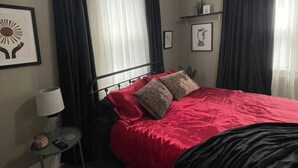 A bedroom with a bed, a nightstand, a lamp, and two windows with curtains. - Cozy vintage getaway minutes from downtown! (Lincoln)