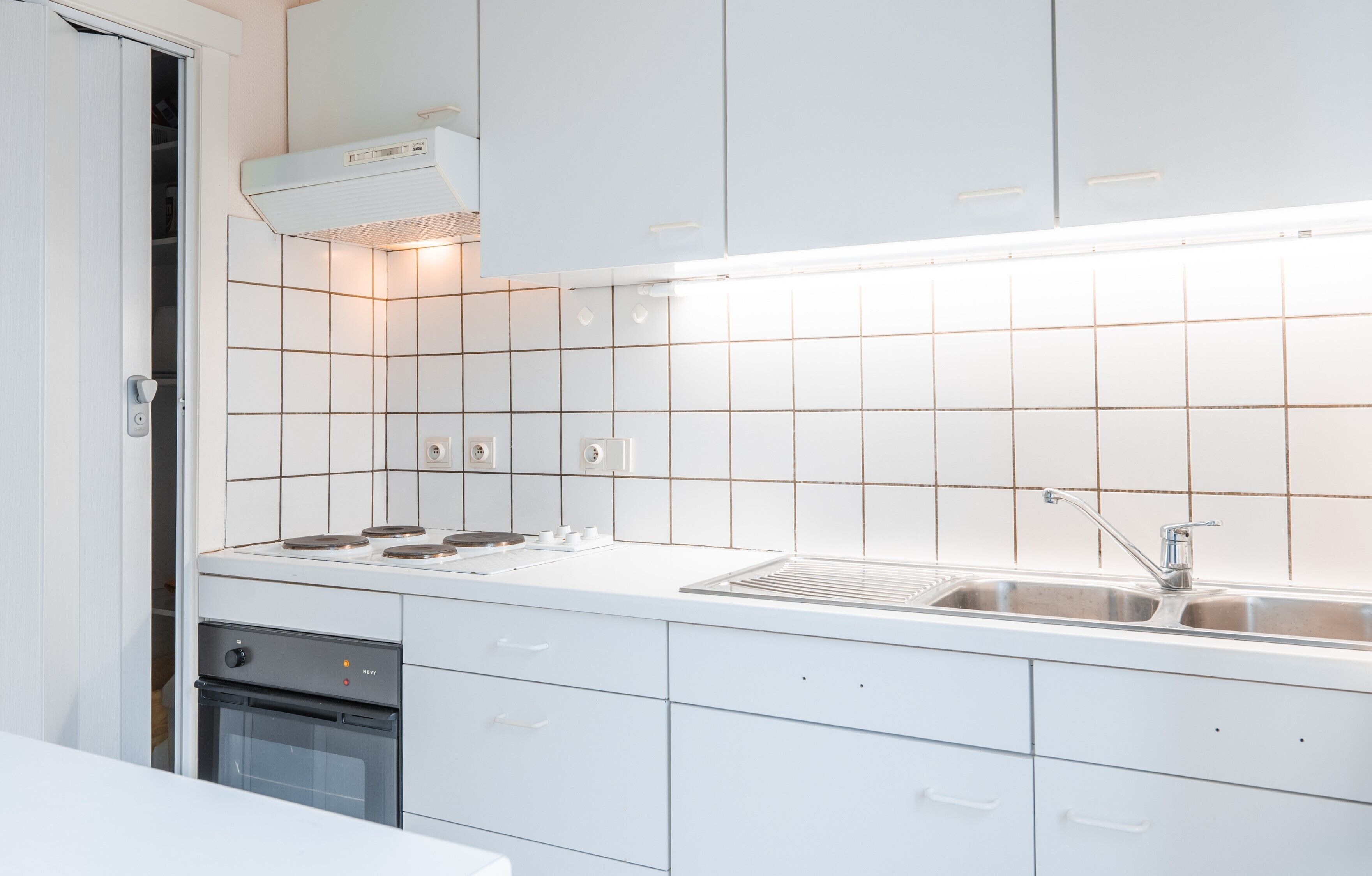 A modern kitchen with white cabinets, a stainless steel sink, and a built-in oven.