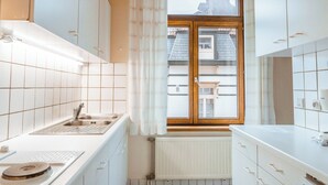 Eine Küche mit weißen Schränken, einem Fenster mit Vorhängen, einer Spüle und einem Heizkörper.