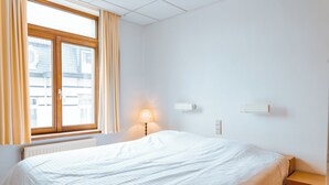 Ein Schlafzimmer mit einem großen Bett, einem Nachttisch, einer Lampe und einem Fenster mit Vorhängen.