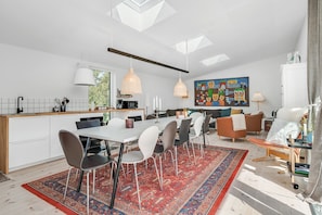 A modern kitchen with a dining area, a large rug, and a colorful painting on the wall.