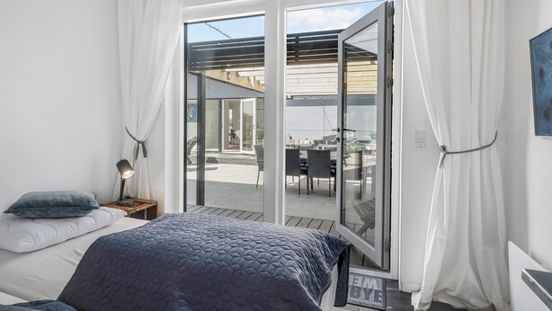 Une chambre à coucher comprenant un lit, une table de chevet, une lampe et une vue sur un patio extérieur, accessible par une porte-fenêtre coulissante.