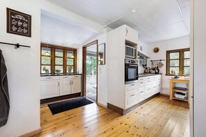 Une cuisine avec des meubles blancs, un four Ă micro-ondes et une cuisiniĂšre. Le sol est en bois et il y a un tapis noir.