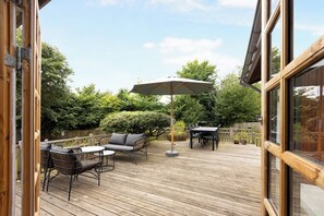 Een houten terras met buitenmeubels, een tafel en een parasol.
