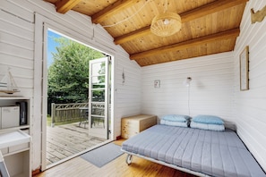 Ein kompakter Raum mit einem Bett, einem kleinen Schreibtisch und einer Tür zu einer Terrasse.