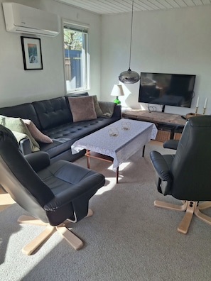 Ein Wohnzimmer mit schwarzem Ledersofa, einem Holztisch, einem schwarzen Lederstuhl, einem Fernseher und einer Lampe.