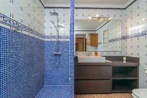 Casa de banho com azulejos de mosaico azuis, chuveiro, pia e espelho.