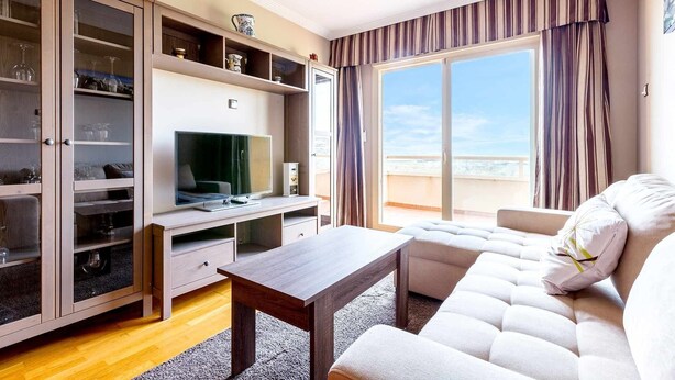 Een moderne woonkamer met een bank, een televisie en een houten kast met glazen deuren.