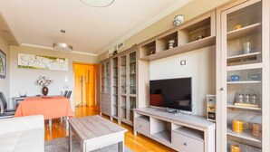 Een moderne woonkamer met een televisie, houten kasten en een eethoek met een tafel en stoelen.