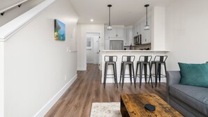 Une cuisine moderne avec des meubles blancs, un îlot central doté de tabourets et des luminaires suspendus.