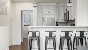 Une cuisine moderne avec des meubles blancs, un réfrigérateur en acier inoxydable et trois tabourets de bar noirs.