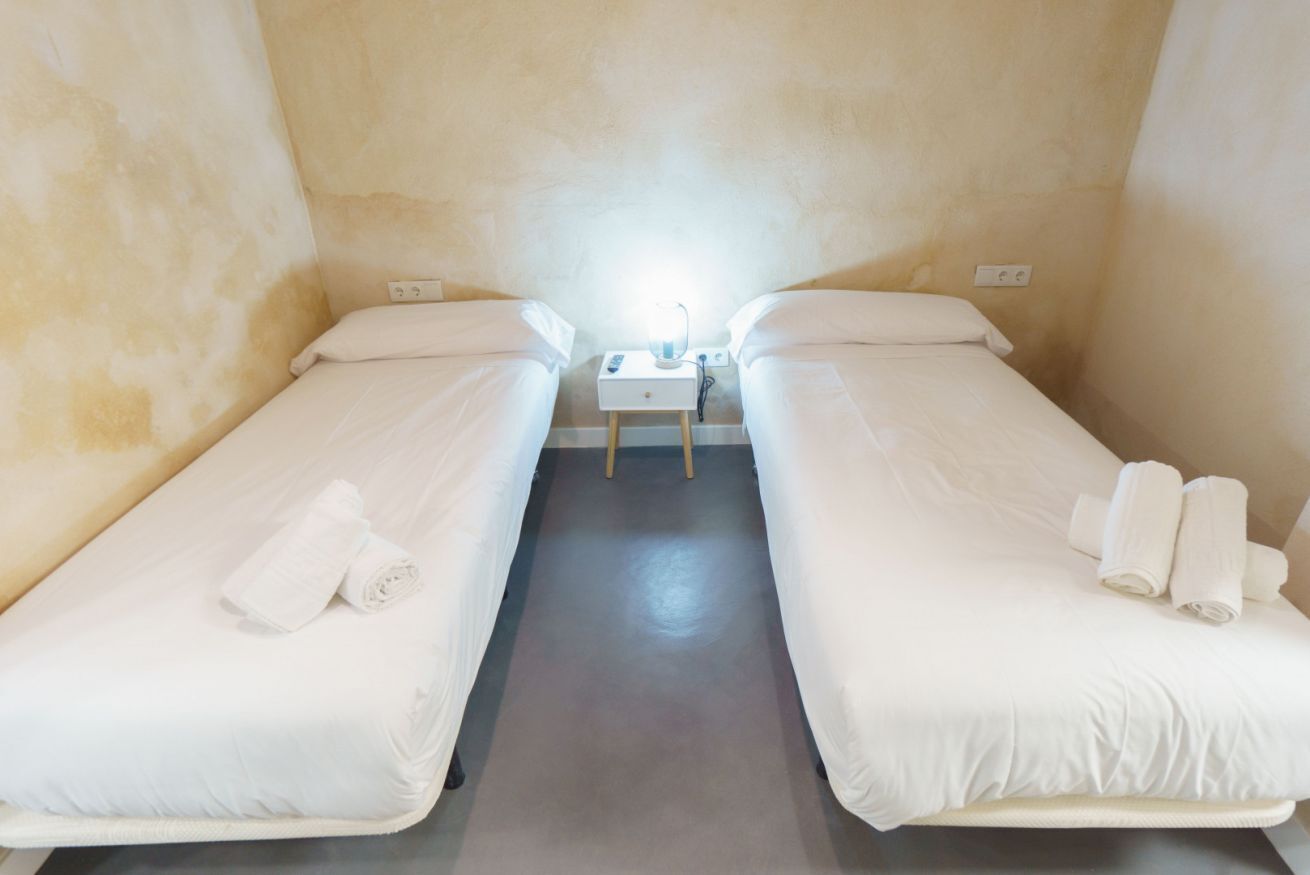 Une petite chambre propre, avec deux lits simples, une table de chevet avec une lampe et des serviettes sur chaque lit.