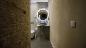 Un couloir étroit mène à une salle de bain équipée de toilettes, d’un lavabo et d’un mur recouvert de carreaux.