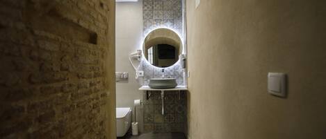 A narrow hallway leading to a bathroom with a toilet, sink, and a tiled backsplash.