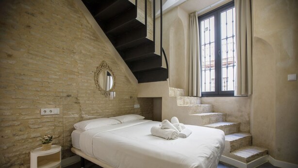 Une chambre à coucher avec un grand lit, un escalier et une fenêtre avec des rideaux.