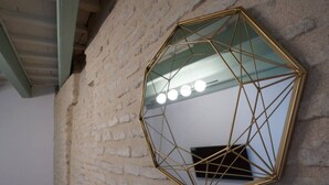 Et sekskantet spejl med geometrisk ramme monteret på en muret mur med struktur.