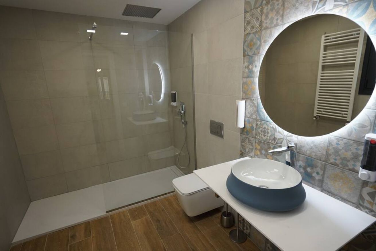 Une salle de bain moderne avec une douche à parois de verre, un lavabo blanc doté d’un receveur bleu et un miroir décoratif.