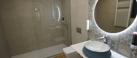 A modern bathroom with a glass-enclosed shower, a white sink with a blue basin, and a decorative mirror.