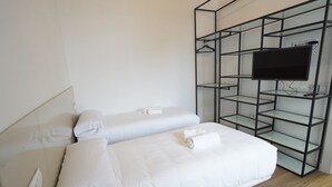 Et hotelværelse med to senge, et fjernsyn på en glashylde og et kontrolpanel på væggen.