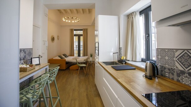 Una cocina compacta con encimera de madera, un lavabo y un hervidor. Hay una zona de comedor con un sofá y sillas.