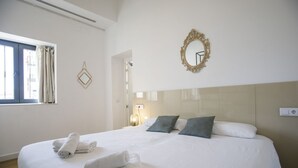 Una cama bien hecha con toallas dobladas, un espejo grande y una ventana con cortinas.