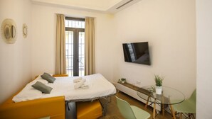 Habitación de hotel pequeña con una cama, televisión, una mesita y zona de estar.