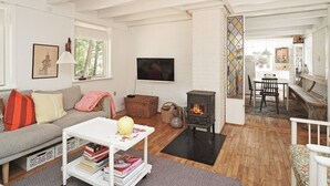 A cozy living room with a sofa, a coffee table with books, a fireplace, and a dining area with a table and chairs.