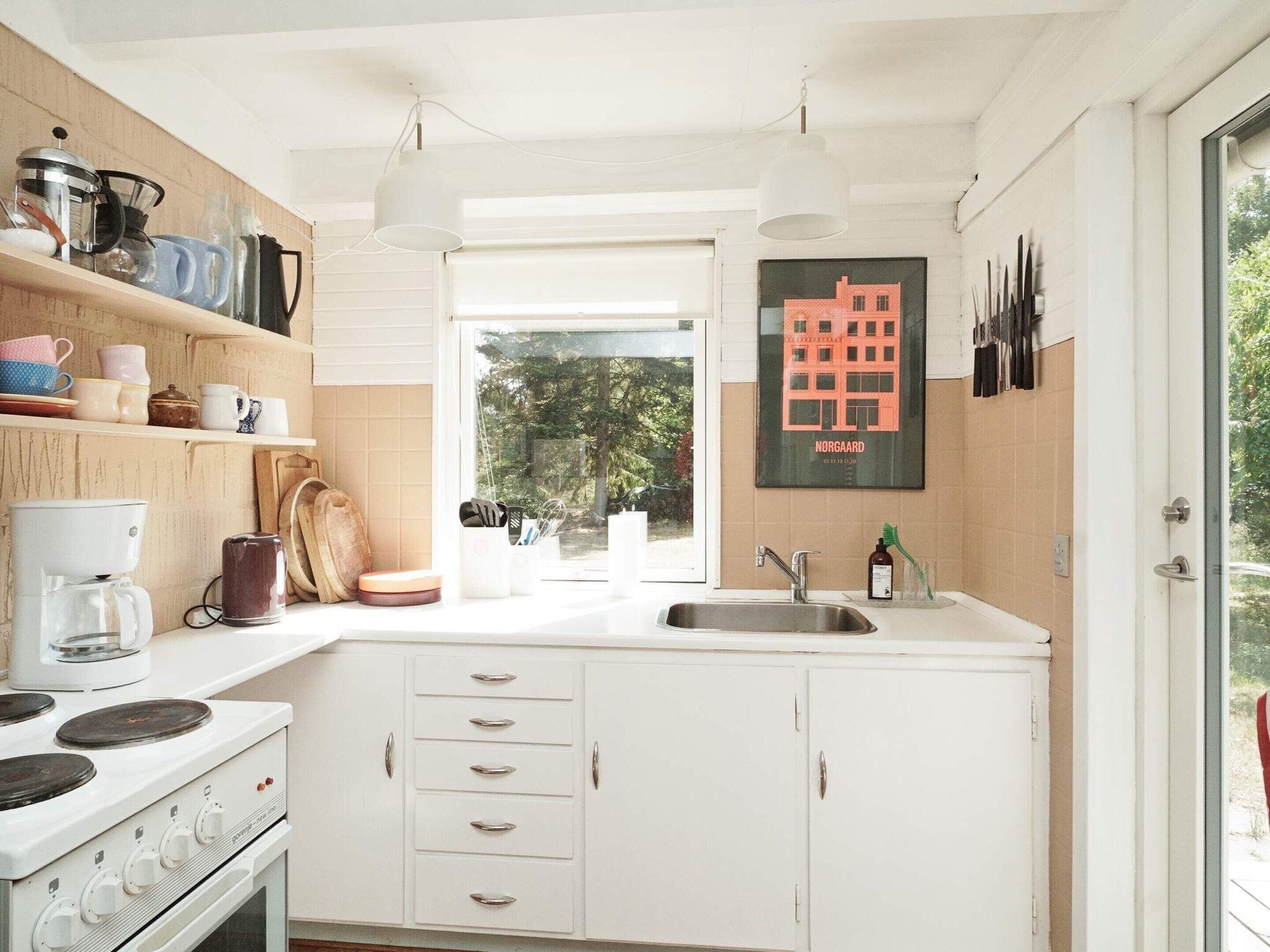 A modern kitchen with white cabinets, a stove, a coffee maker, and a window with a view of trees.