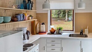 A modern kitchen with white cabinetry, a stove, and a window offering a view of the outdoors.